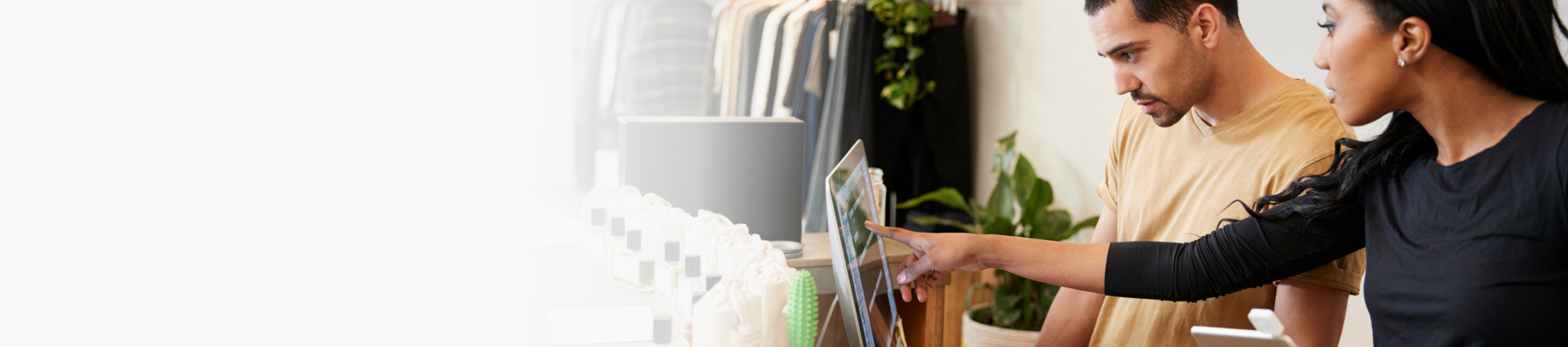 Two people collaborating on a computer and tablet in a clothing retail store setting.