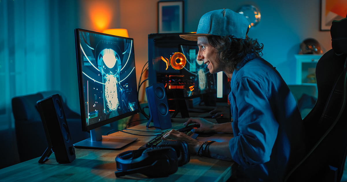 A young man smiles while playing an online game on a desktop computer setup